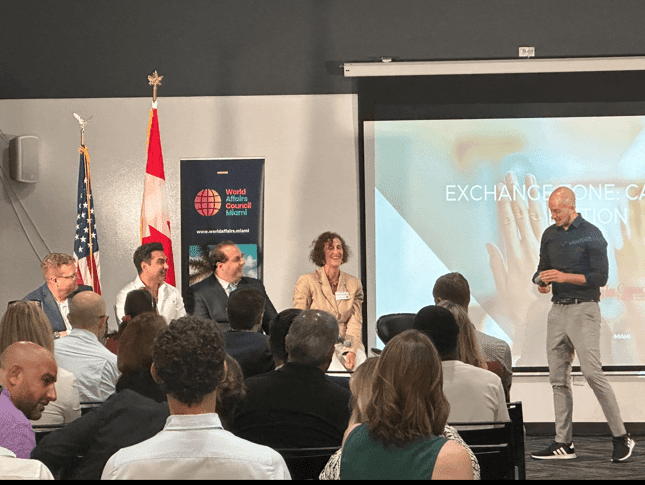 Panel discussion at Canadian Innovation Night hosted by the World Affairs Council in Miami, featuring multiple speakers and a presentation backdrop, with flags of the USA and Canada visible.