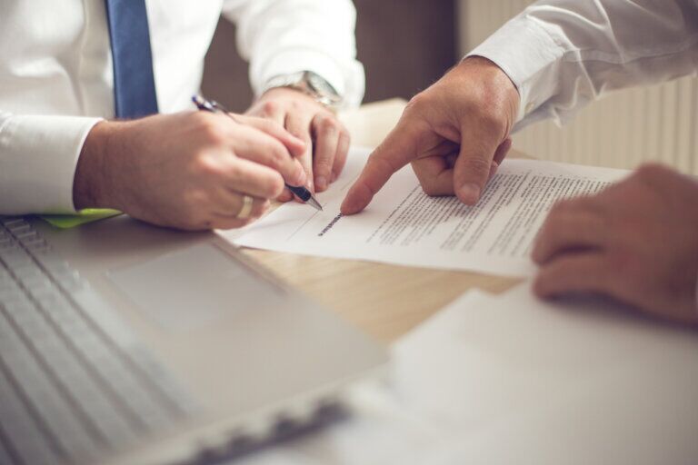 Hands signing a document and pointing at text, symbolizing international licensing agreements and business negotiations.